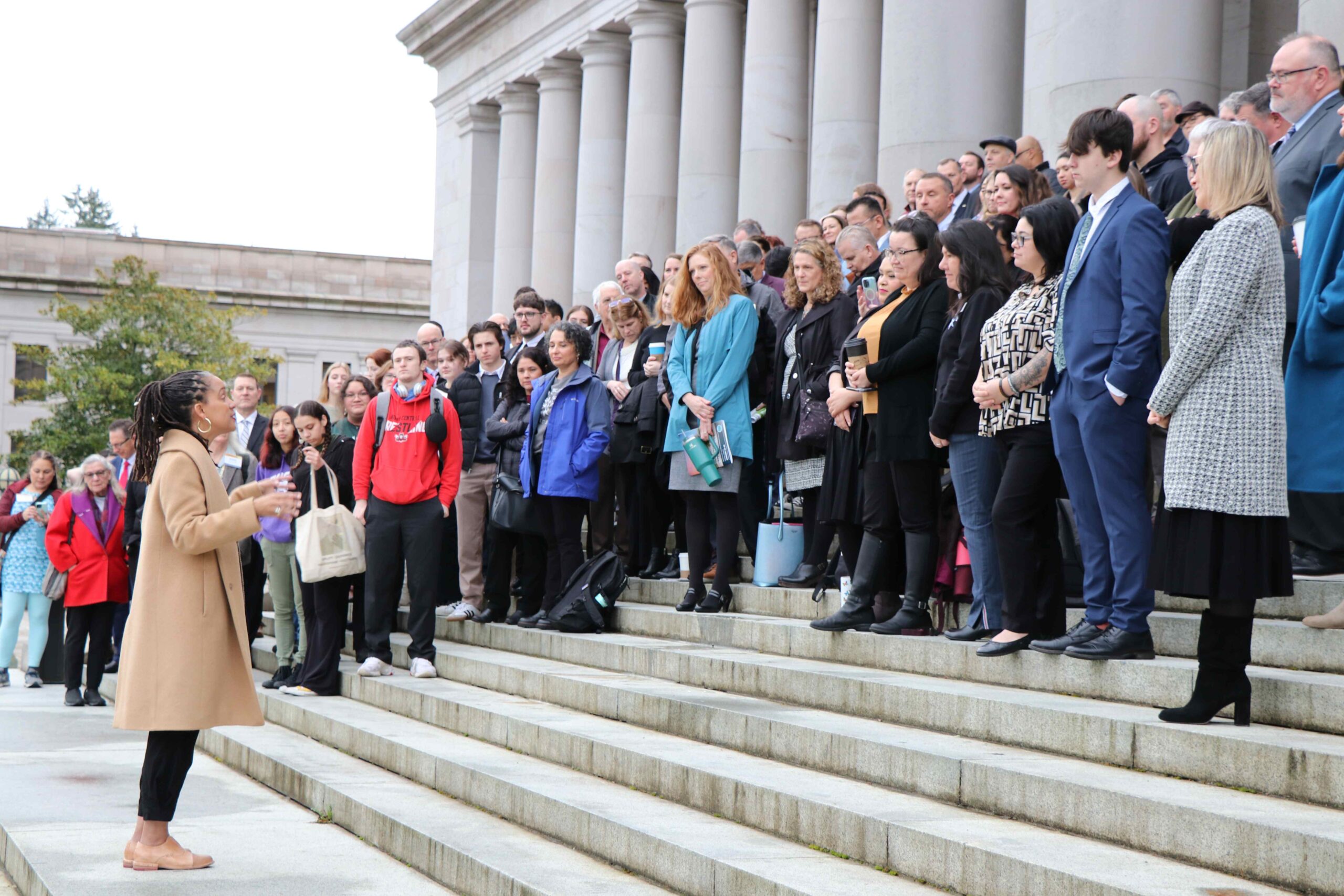 Several board members standing on the Capitol building steps listening to Legislator April Berg